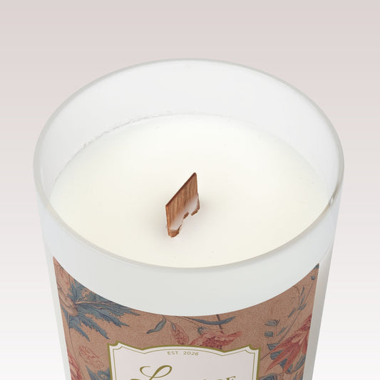 A close-up top view of a white candle in a frosted glass jar with a single wooden wick.