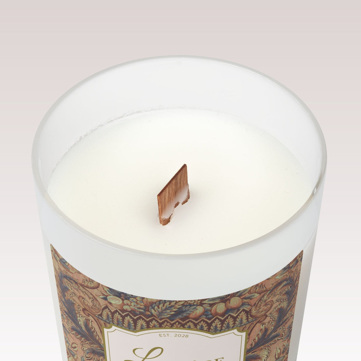 A close-up top view of a white candle in a frosted glass jar with a single wooden wick. 